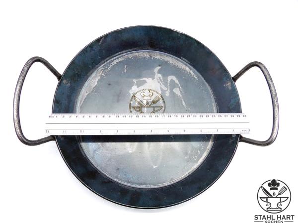 Eisenpfanne mit zwei Griffen, darauf liegt ein Lineal
